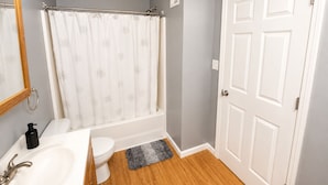 A bathroom with a white bathtub, a toilet, a sink, and a door. - Close to stadiums and downtown. Pets Welcome: Beautifully remodeled 2 BR Home (Independence)