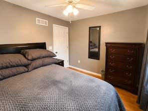 Un dormitorio con cama, cómoda, ventilador de techo y una puerta.