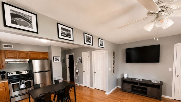 A modern kitchen with stainless steel appliances, a dining area with a table and chairs, a ceiling fan, and a flat-screen TV mounted on the wall. - Close to stadiums and downtown. Pets Welcome: Beautifully remodeled 2 BR Home (Independence)