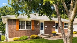 A two-story house with a brick exterior, a front door, and a small front yard with a tree and yellow flowers. - Close to stadiums and downtown. Pets Welcome: Beautifully remodeled 2 BR Home (Independence)