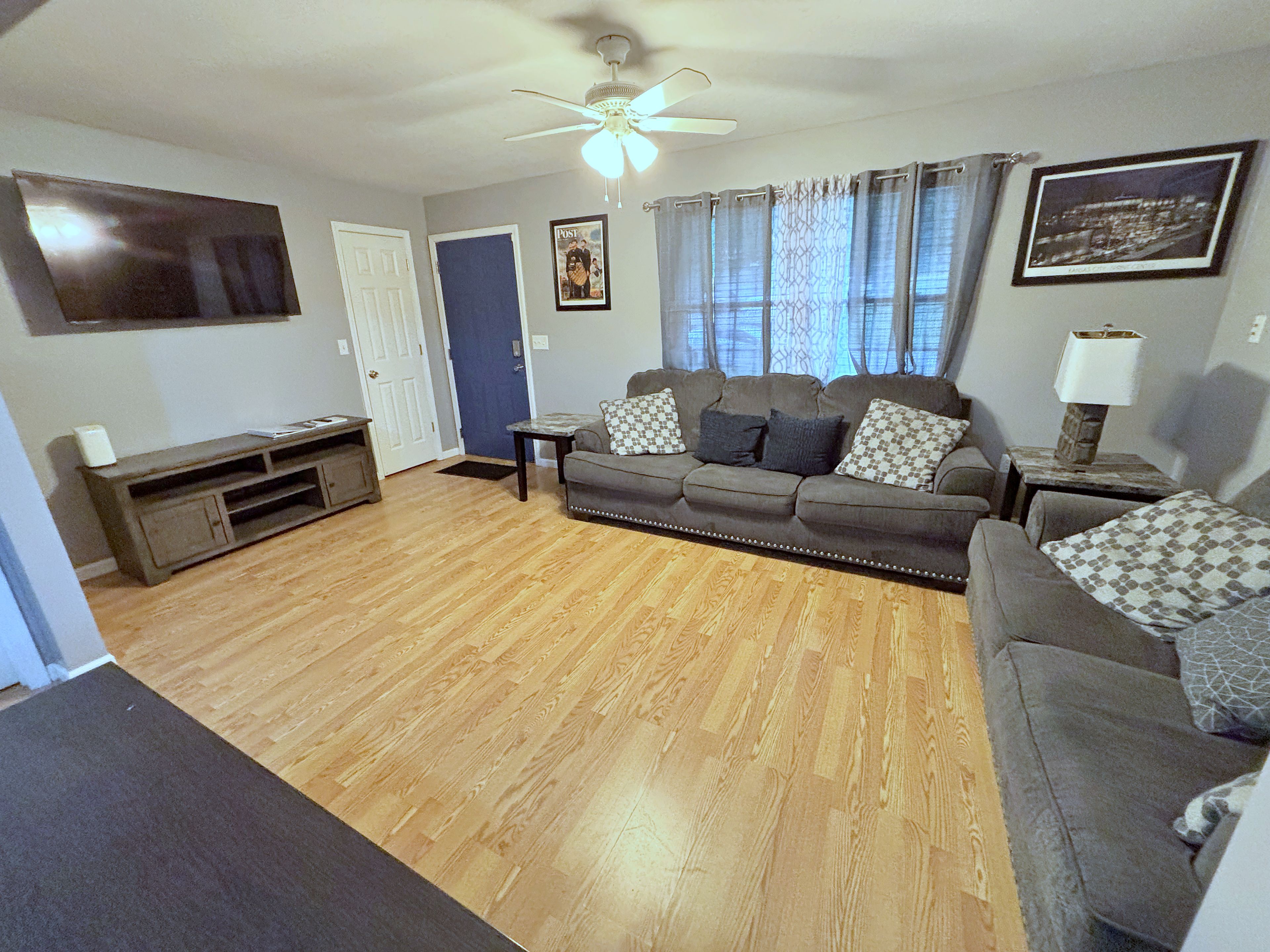 A living room with a sofa, a television, a ceiling fan, and a door.