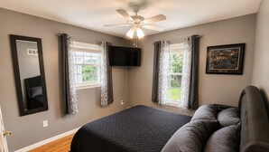 A bedroom with a bed, a ceiling fan, two windows with curtains, a mounted TV, and a framed picture on the wall. - Close to stadiums and downtown. Pets Welcome: Beautifully remodeled 2 BR Home (Independence)