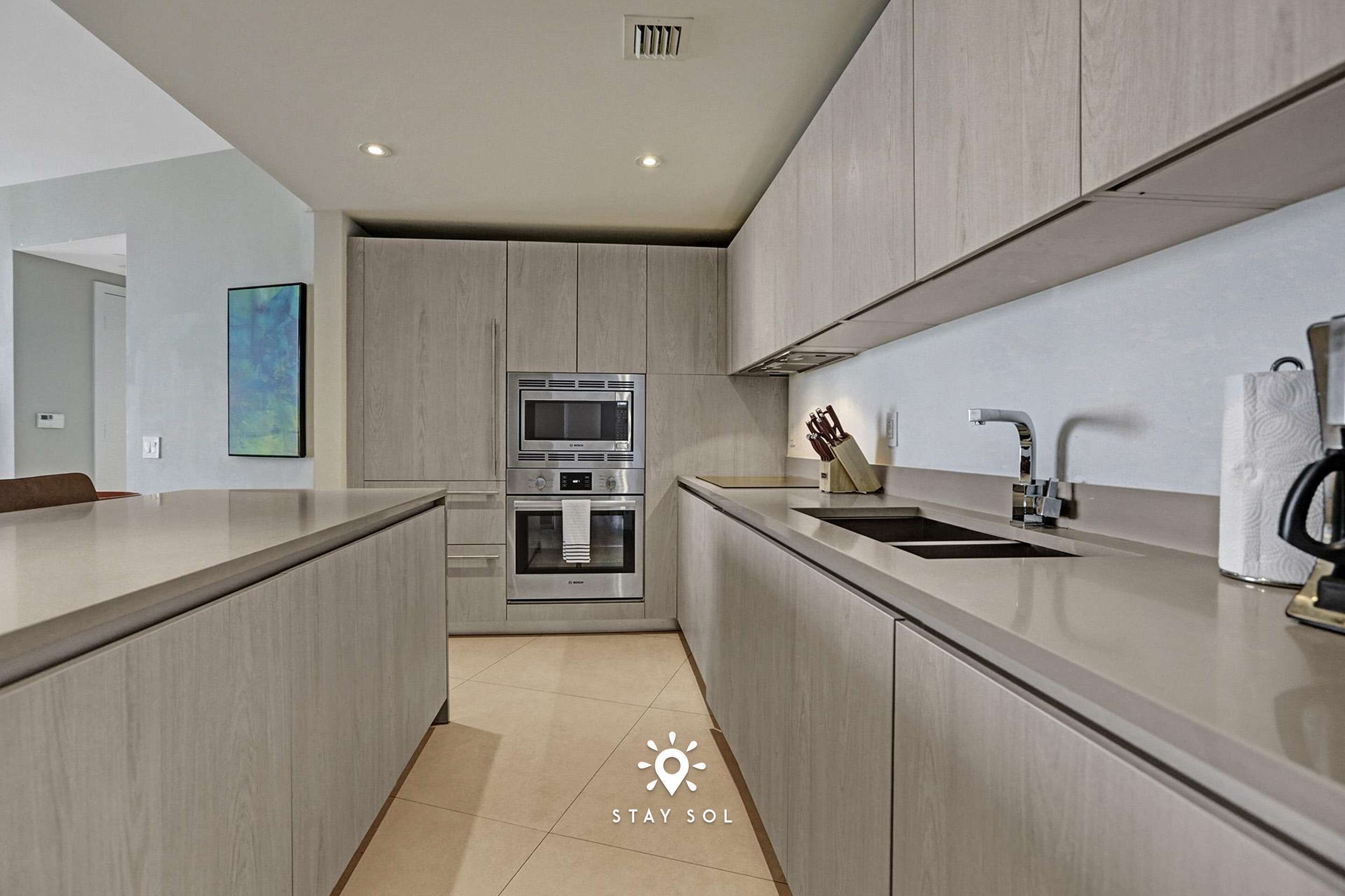 A modern kitchen with a central island, built-in oven, and stainless steel appliances.