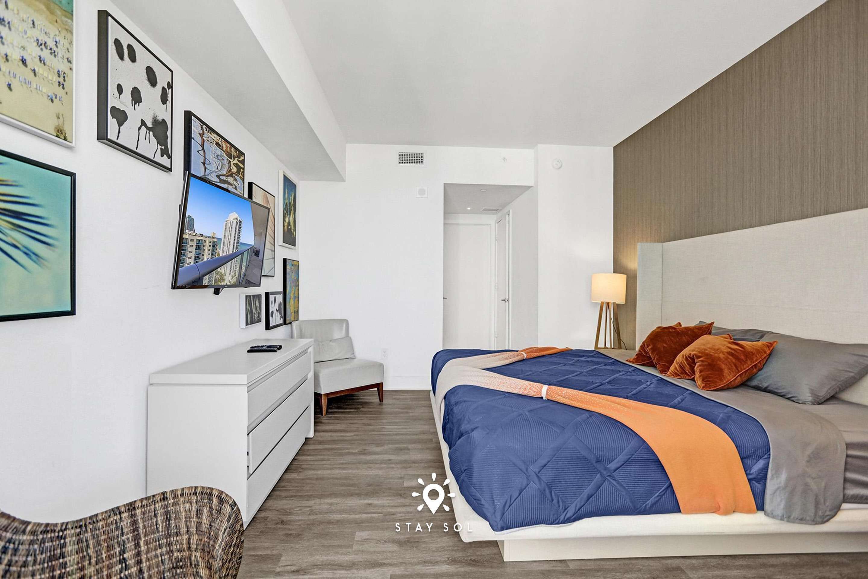 Una habitación de hotel moderna con cama, escritorio y silla. Incluye obras de arte en las paredes y un televisor.