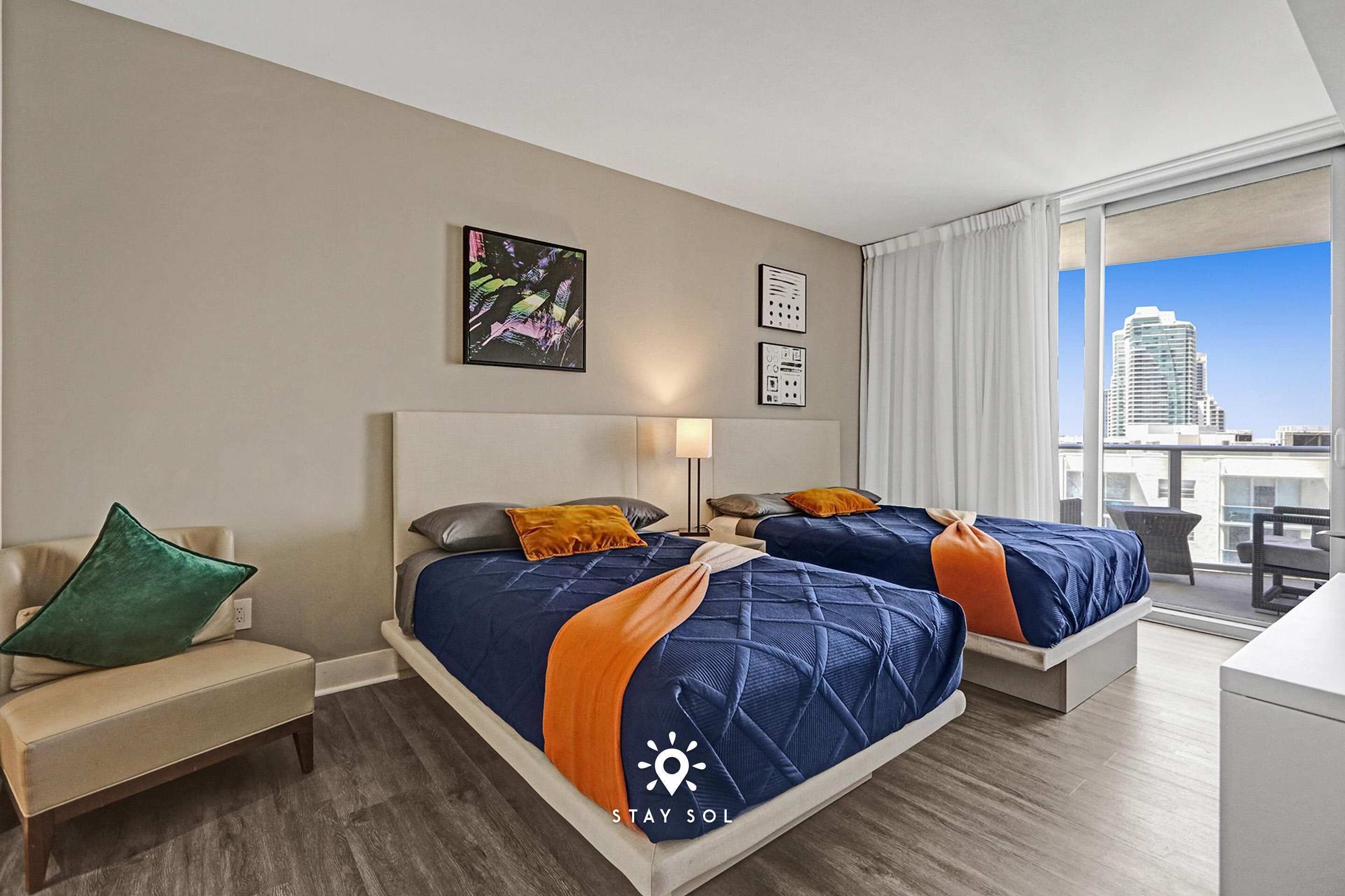Camera d'hotel con due letti, una poltrona letto, una scrivania e una grande finestra vista città.