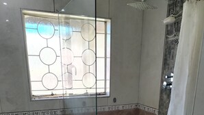 A bathroom with a glass shower enclosure, a toilet, and a window with a geometric pattern. - J & J Paradise Guesthouse  (Pietermaritzburg)