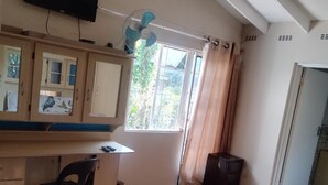 A bedroom with a bed, a desk, a chair, a television, a window with curtains, and a ceiling fan. - J & J Paradise Guesthouse  (Pietermaritzburg)