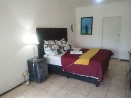 Un dormitorio con cama, mesita de noche, lámpara y un cuadro en la pared.
