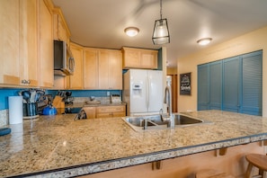 Cocina con encimeras de granito, armarios de madera y pileta de acero inoxidable, además de un refrigerador.