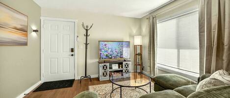 A living room with a sofa set, a flat-screen TV, a coat rack, and a window with curtains.
