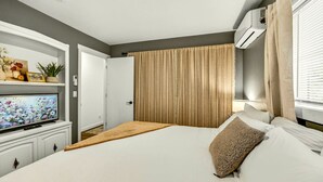 Een slaapkamer met een bed, een televisie op een dressoir, een raam met gordijnen en een airconditioning.