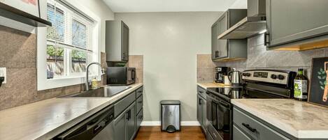 A compact kitchen with a window, stainless steel appliances, and a trash bin.