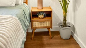 Un dormitorio con una cama, una mesita de noche con lámpara, una planta en maceta y tres espejos fijados a la pared.