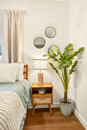 Ein Schlafzimmer mit einem Bett, einem Nachttisch mit Lampe, einer Topfpflanze und drei Wandspiegeln.