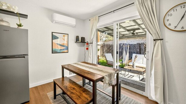 Una cocina compacta con refrigerador, una mesa de comedor con bancos, aire acondicionado de pared y un reloj.