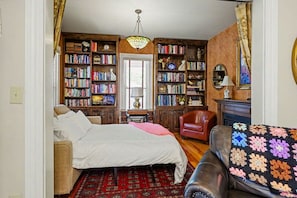 Une pièce confortable avec un lit, un fauteuil rouge, une bibliothèque et un tapis à motifs.