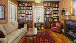 A living room with a sofa, a red armchair, a fireplace, and bookshelves filled with books.