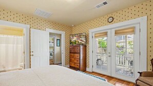 A bedroom with a large bed, a dresser, a mirror, and a door leading to a balcony.