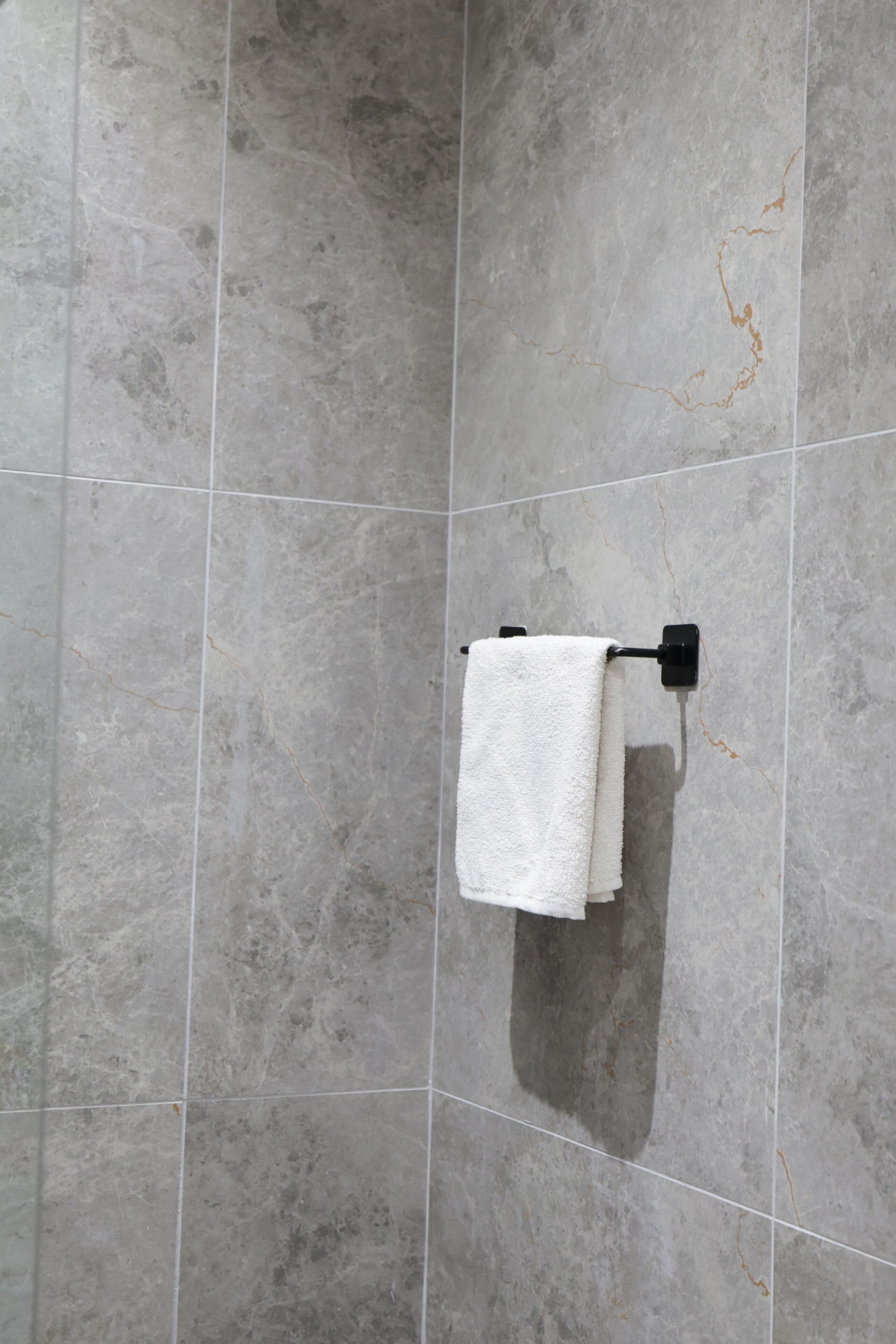 A bathroom with grey tiled walls and a white towel hanging on a black towel rack.