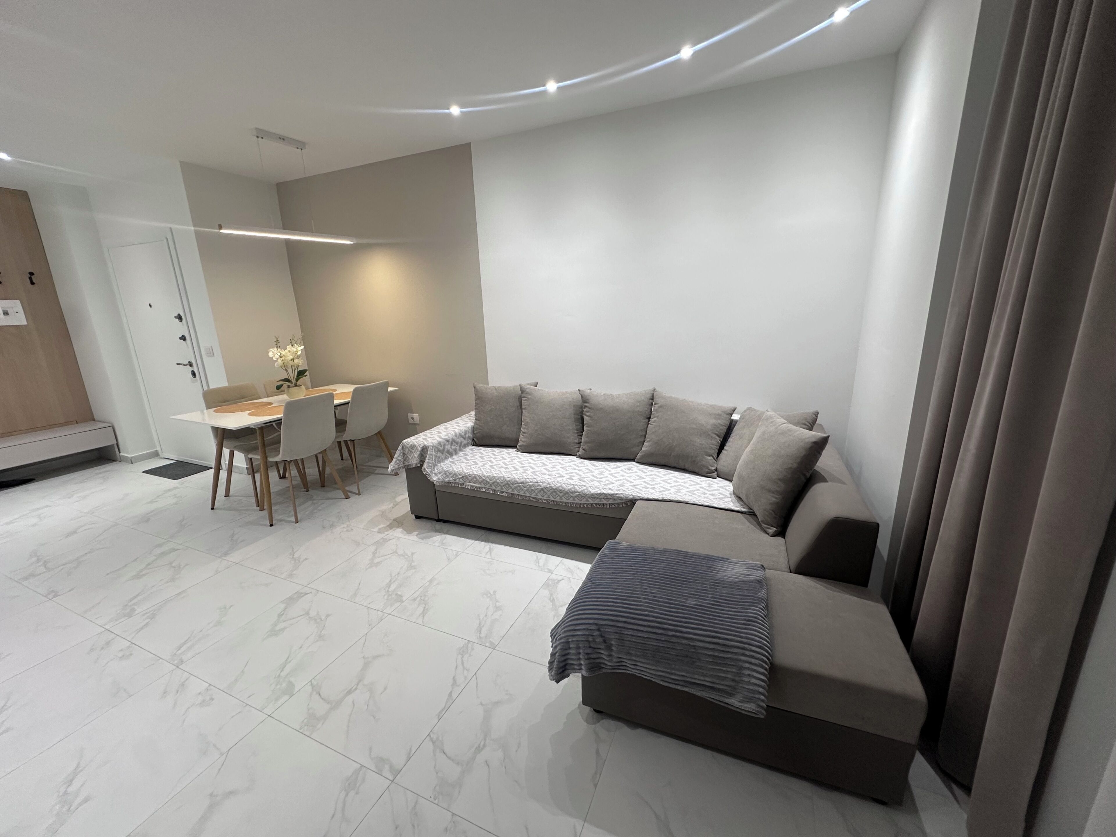 A modern living room with a sofa, a dining table, and a small kitchen area.
