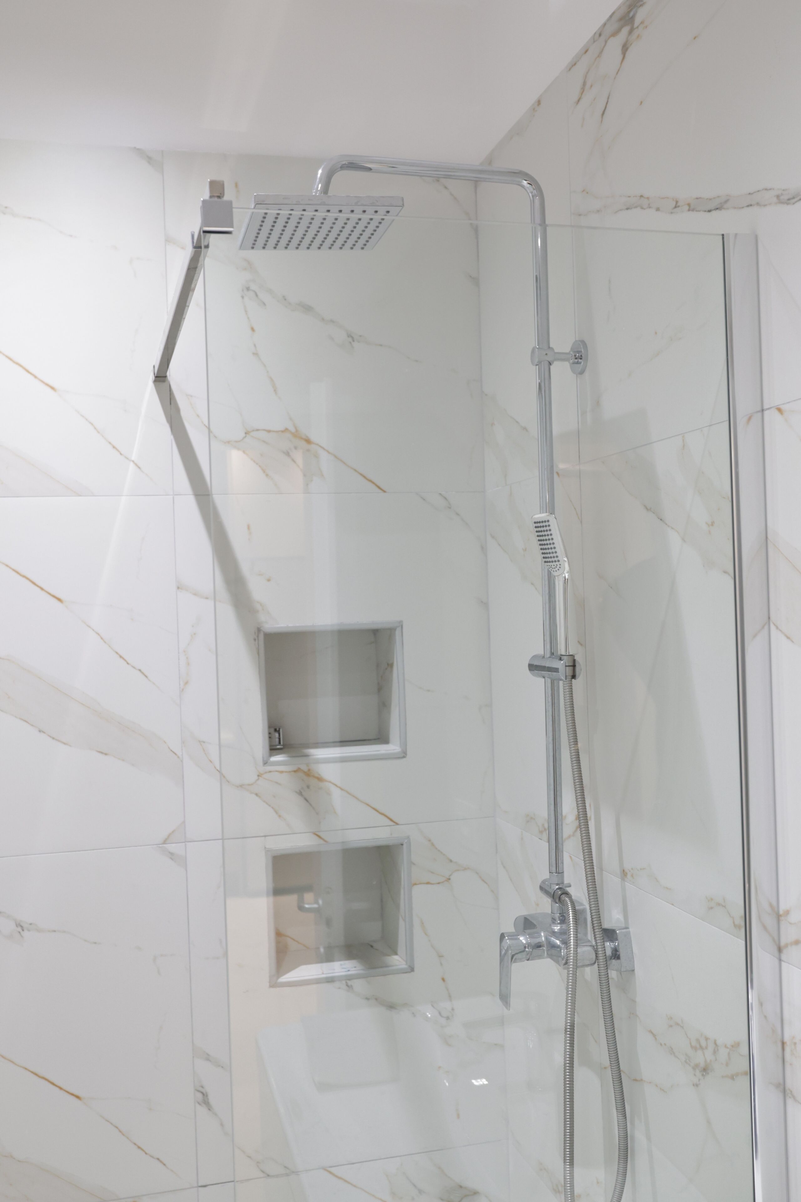 A shower with a handheld showerhead, a handheld shower attachment, and a wall-mounted showerhead.