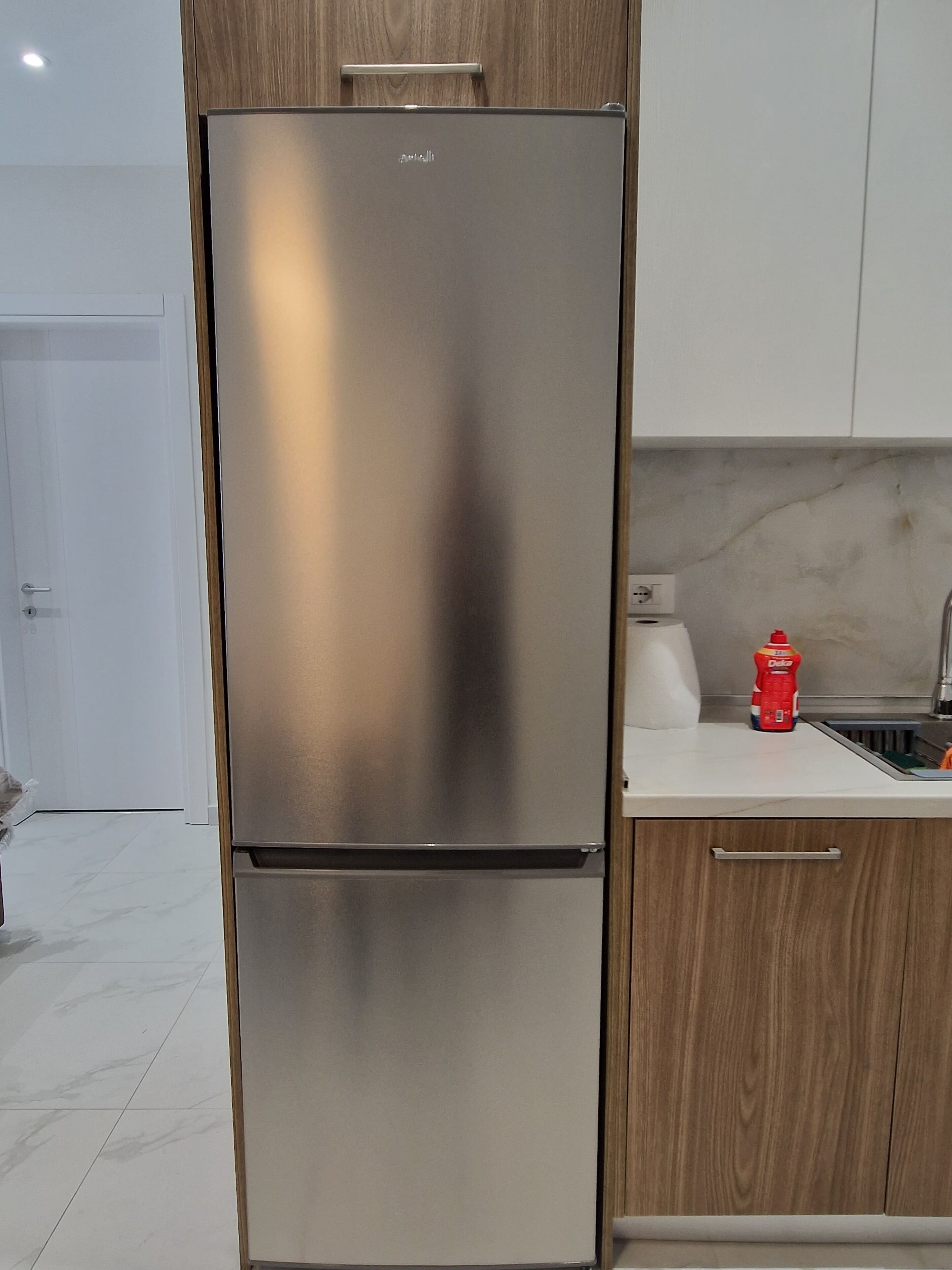 A stainless steel refrigerator in a kitchen with wooden cabinets and a marble countertop.