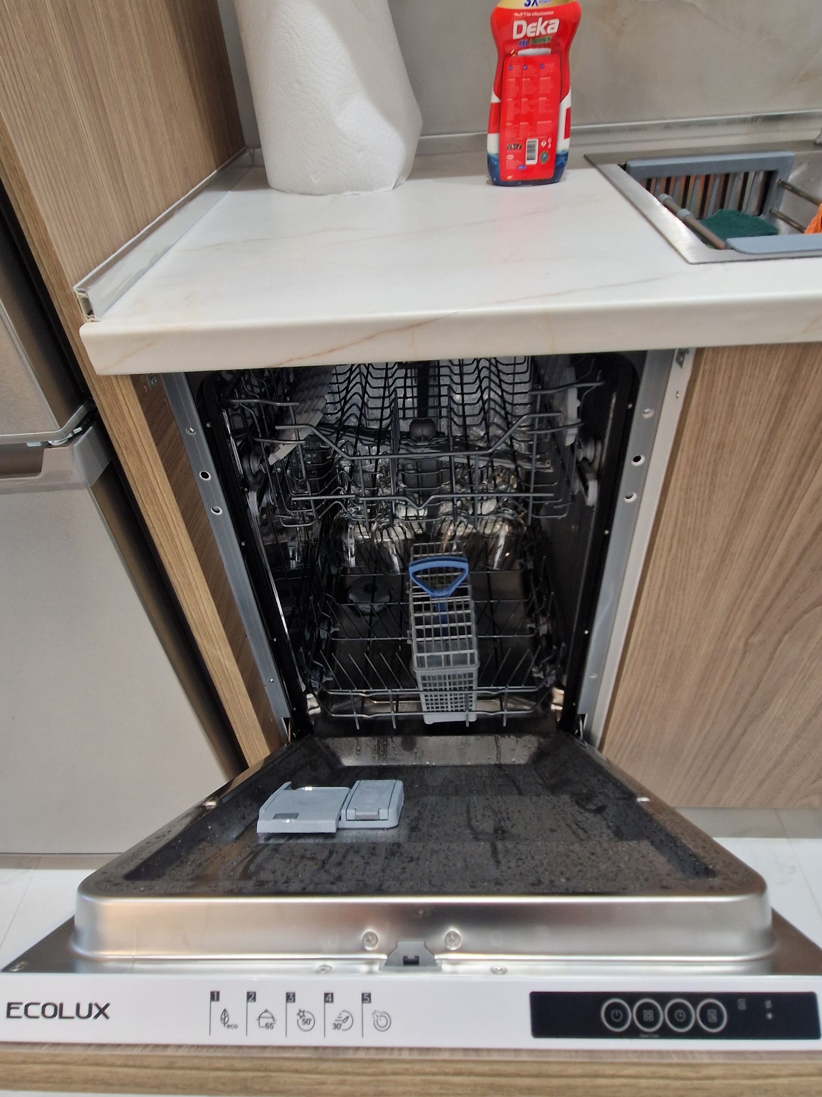 An open dishwasher with a detergent bottle on top, a dish rack inside, and control panel with various buttons and indicators.