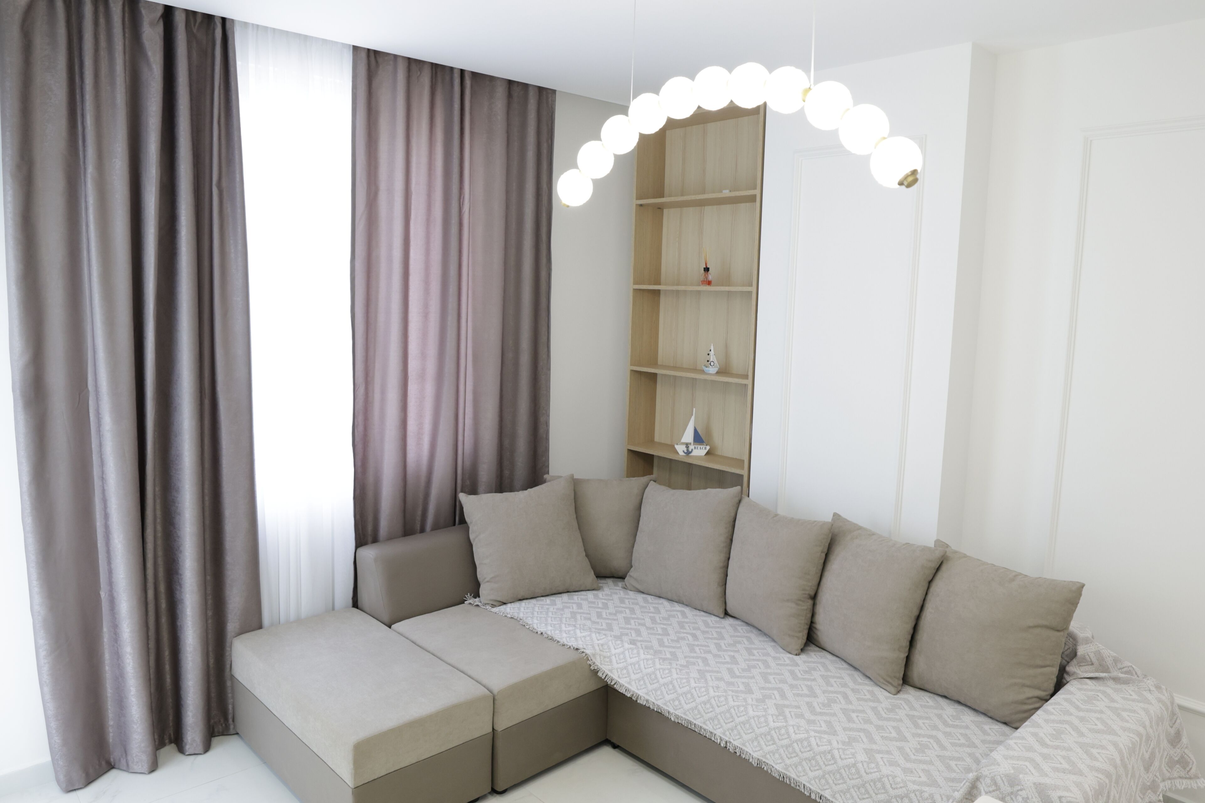 A modern living room with a sectional sofa, a built-in shelving unit, and a pendant light.