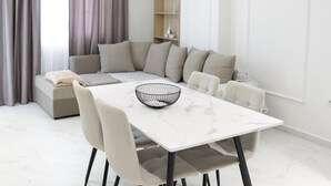 Un espace repas moderne avec une table et des chaises blanches, un canapé et un luminaire suspendu.