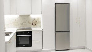 Une cuisine moderne avec des meubles blancs, un réfrigérateur en acier inoxydable et un four encastré.