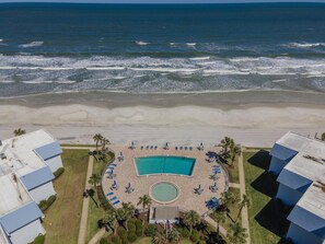 Luftaufnahme eines Hotels direkt am Strand mit Schwimmbad, Liegestühlen und Palmen.