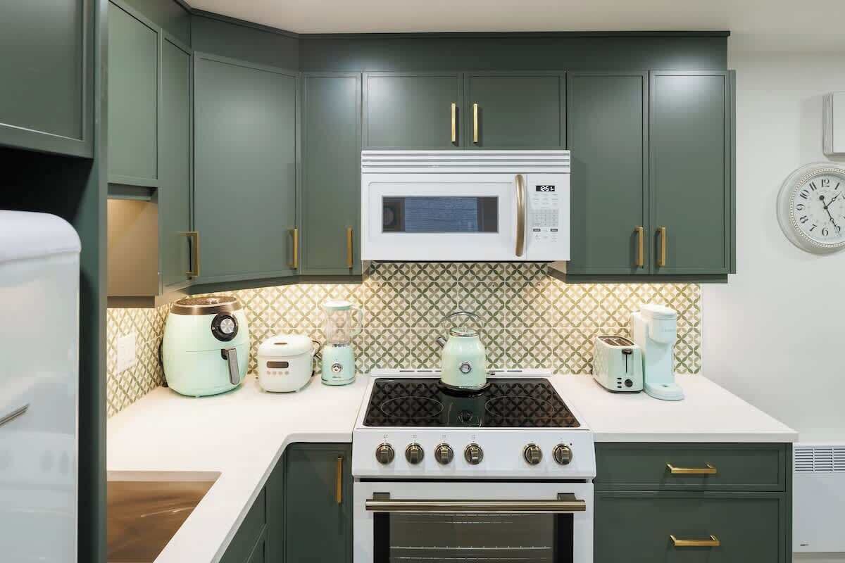 Une cuisine avec des meubles de couleur verte, une cuisinière blanche, un four à micro-ondes et divers appareils électroménagers sur le plan de travail.