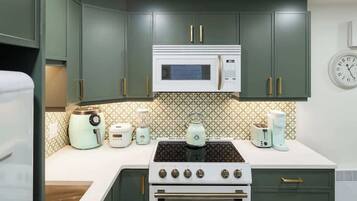 Une cuisine avec des meubles de couleur verte, une cuisinière blanche, un four à micro-ondes et divers appareils électroménagers sur le plan de travail.