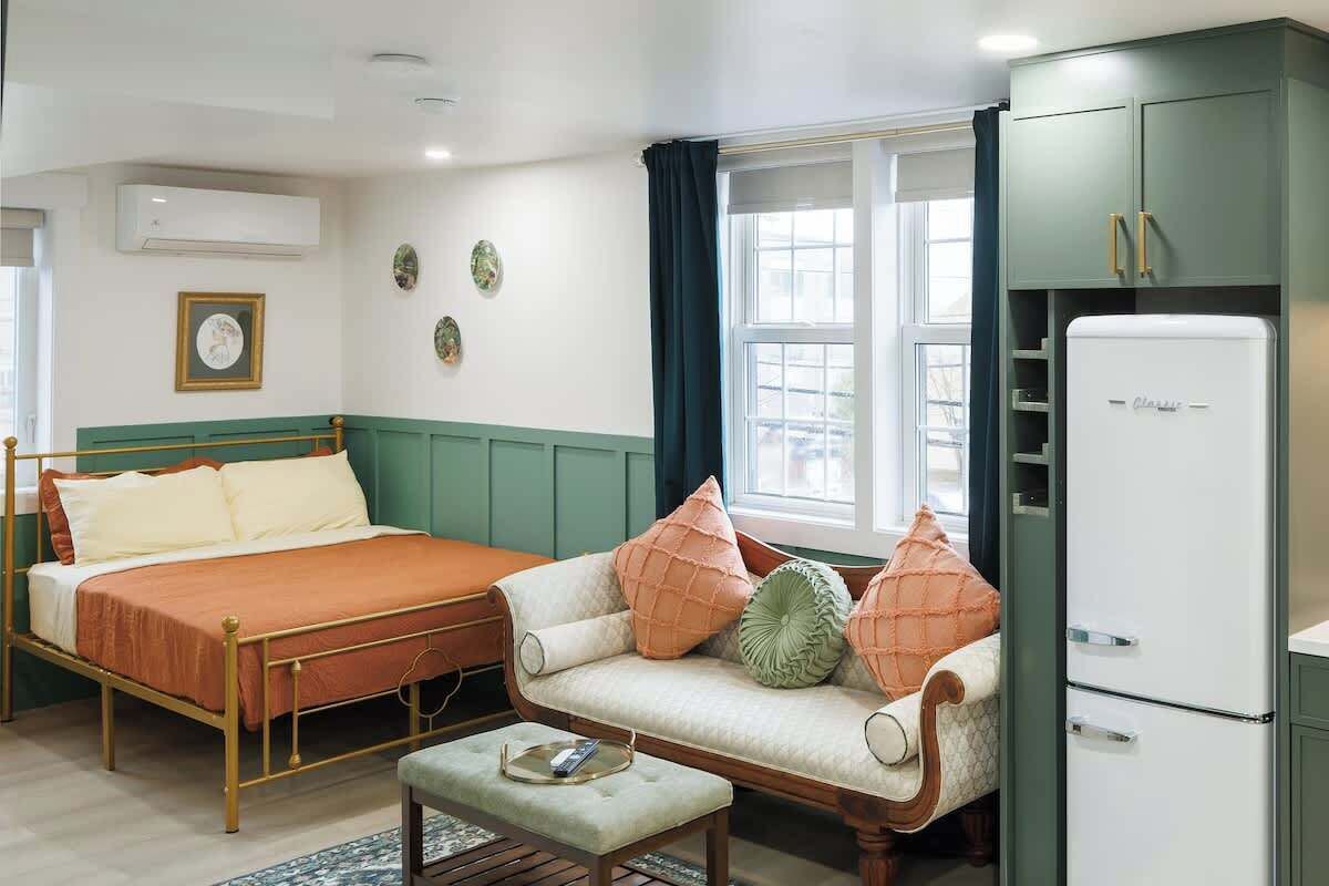 Un dormitorio con cama, sofá, mesita y refrigerador.