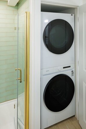 A laundry room with two stacked washing machines, a glass shower enclosure, and a white tiled wall. - Green Gables Suite - Studio in Downtown (Charlottetown)