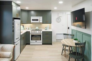 A compact kitchen with a microwave, oven, and a dining area with chairs and a table. - Green Gables Suite - Studio in Downtown (Charlottetown)