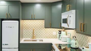 Une cuisine avec des meubles de couleur verte, un réfrigérateur blanc, un four à micro-ondes et une cuisinière.