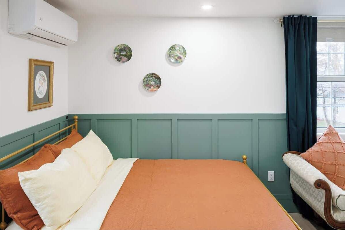 Un dormitorio con cama, una silla, un ventanal con cortinas y adornos en la pared.