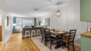 A dining area with a wooden table, chairs, and a hanging light fixture. - Beach Bliss: Charming 3-Bedroom Home (Brackley)