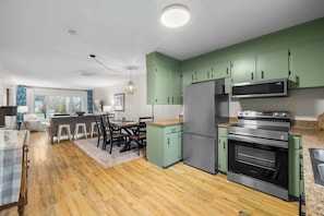 A modern kitchen with green cabinets, a stainless steel refrigerator, and an oven. - Beach Bliss: Charming 3-Bedroom Home (Brackley)
