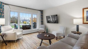 A living room with a sofa, chairs, a coffee table, a TV, and a large window with curtains. - Beach Bliss: Charming 3-Bedroom Home (Brackley)
