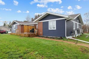 A two-story house with a deck, a covered porch, and a small front yard. - Beach Bliss: Charming 3-Bedroom Home (Brackley)