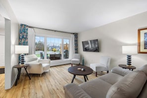 A modern living room with a sofa, two armchairs, a coffee table, and a TV mounted on the wall. - Beach Bliss: Charming 3-Bedroom Home (Brackley)