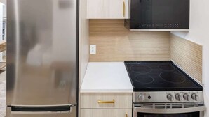 Eine Küche mit einem Edelstahl-Kühlschrank, einer schwarzen Mikrowelle, einem Herd und Holzschränken.