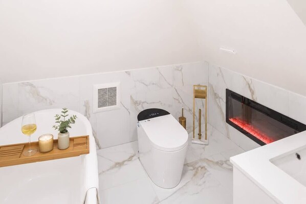 A modern bathroom with a toilet, a sink, a mirror, a wall-mounted heater, and a small plant on the counter.