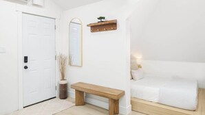 Ein Schlafzimmer mit einem Bett, einer Bank, einem Spiegel und einem regal mit Beleuchtung.