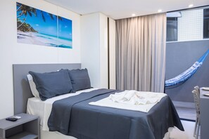 Ein modernes Hotelzimmer mit Bett, Nachttisch, Hängematte und einem großen Fenster mit Vorhängen.