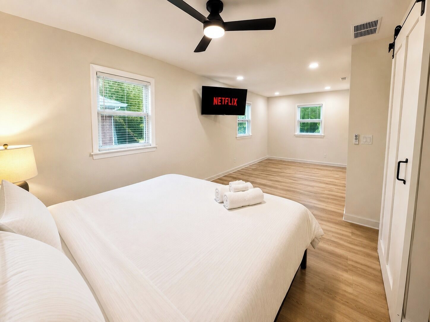 A hotel room with a bed, a ceiling fan, a TV screen displaying Netflix, and a wardrobe.