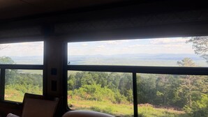 Una habitación con grandes ventanales que ofrecen vistas a un bosque y montañas distantes.