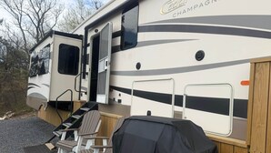 Un vehículo recreativo con una parrilla cubierta, asientos exteriores y una puerta abierta al costado.